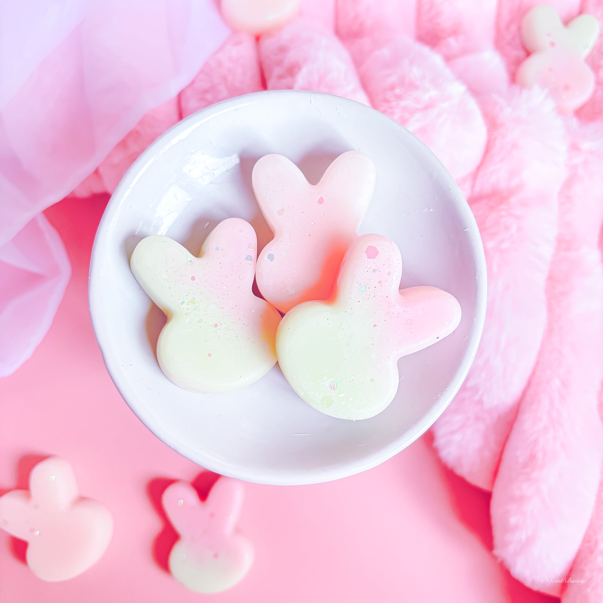 Pastel-colored bunny-shaped candies in a white bowl on a pink background